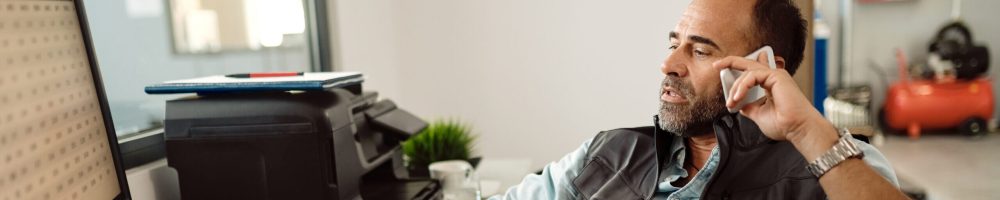 Auto repair man communicating over mobile phone while sitting in office at his workshop.